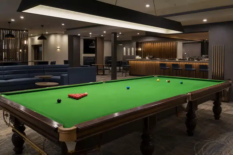Empty hospitality-club snooker room with table lighting, lounge seating, and bar area