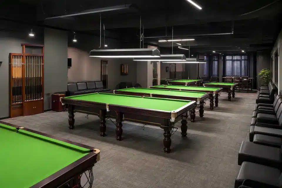 Empty billiards venue layout with spaced tables, cue storage, spectator seating, and overhead lighting